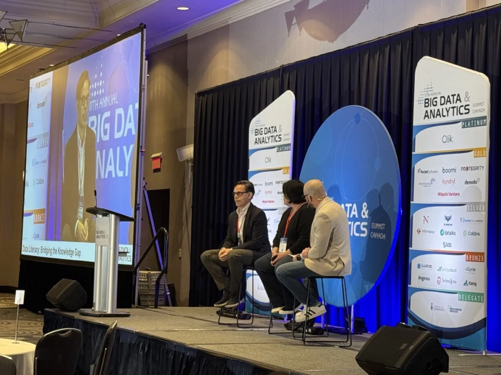 David Legendre, the leftmost panelist (dark hair, glasses, dark blazer), on stage at the 11th Annual Big Data & Analytics Summit Canada. The screen reads “Data Literacy: Bridging the Knowledge Gap.” Two other panelists sit to his right.