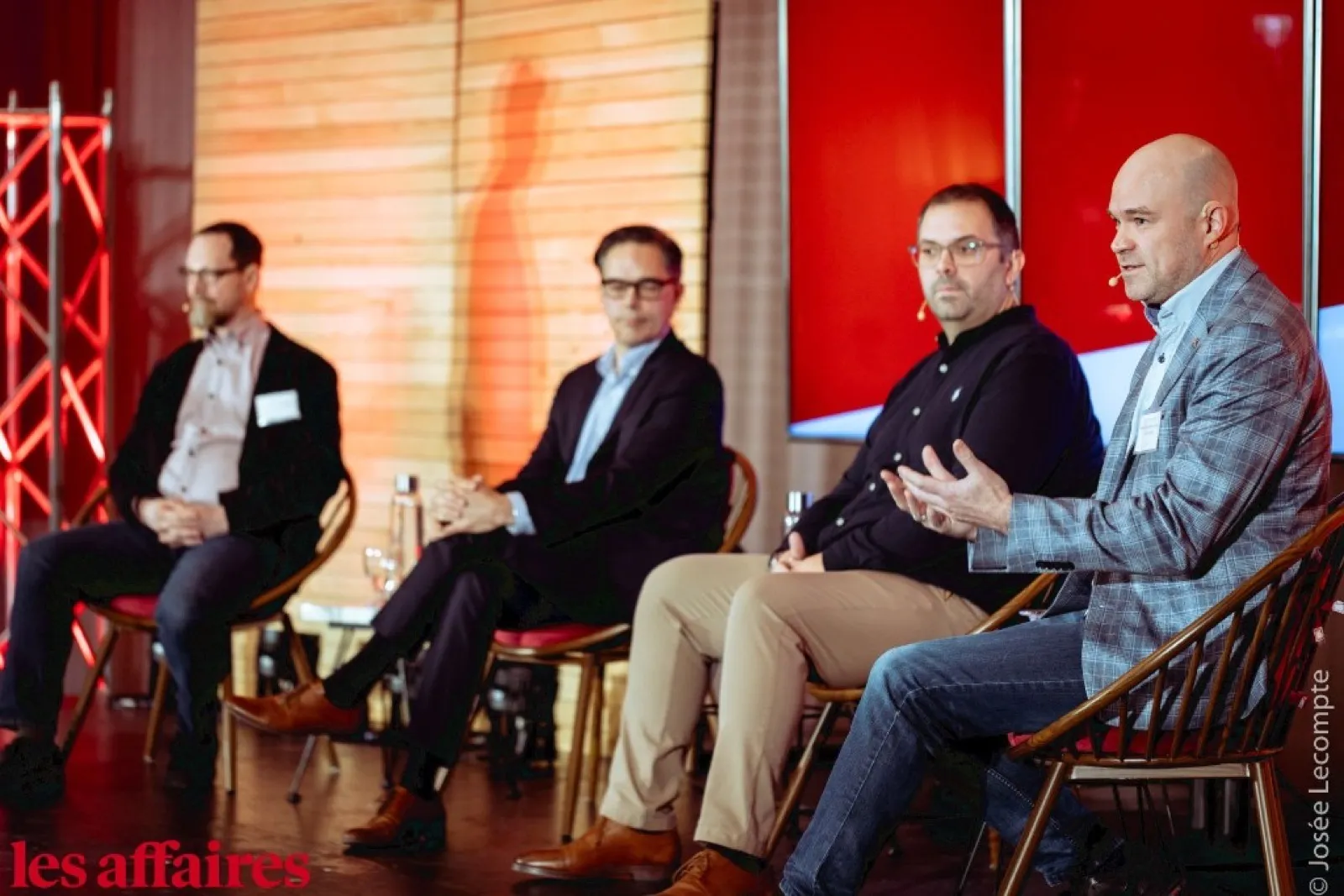 Les Affaires panel: four men seated on stage. David Legendre is second from the left (dark hair, glasses, dark blazer, legs crossed), listening. The bald man on the far right is the one speaking. Photo © Josée Lecompte.